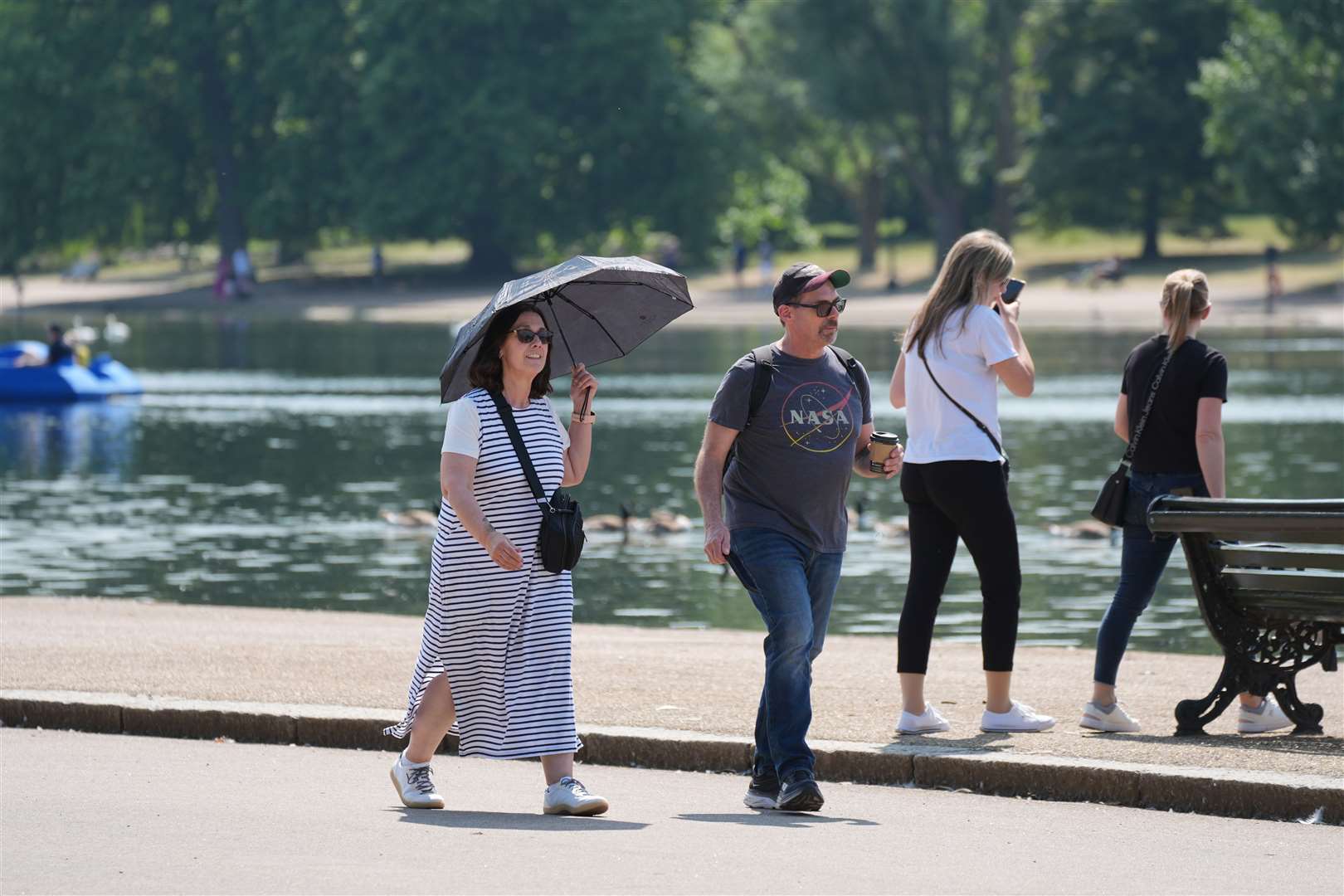 A woman shielding from the sun under an umbrella while a man protects his head from UV rays with a baseball cap (Yui Mok/PA)