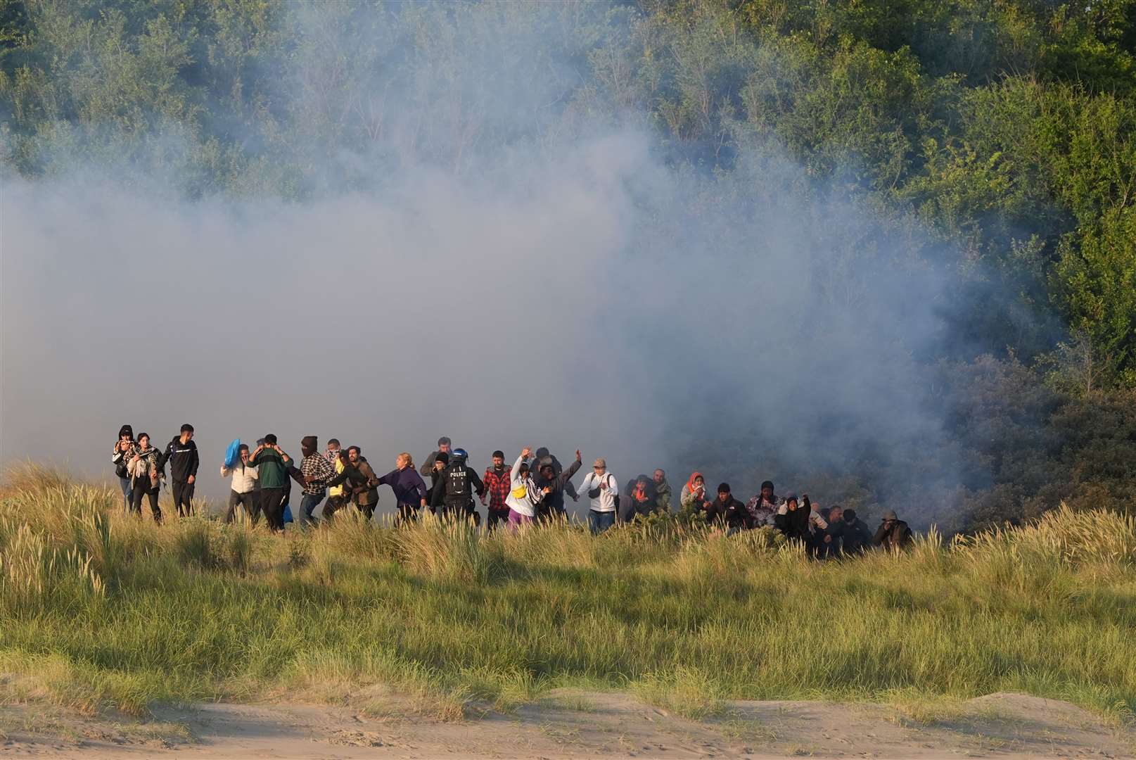 People thought to be migrants emerge from bushes on a beach in Gravelines, France, after French authorities had fired tear gas (Gareth Fuller/PA)