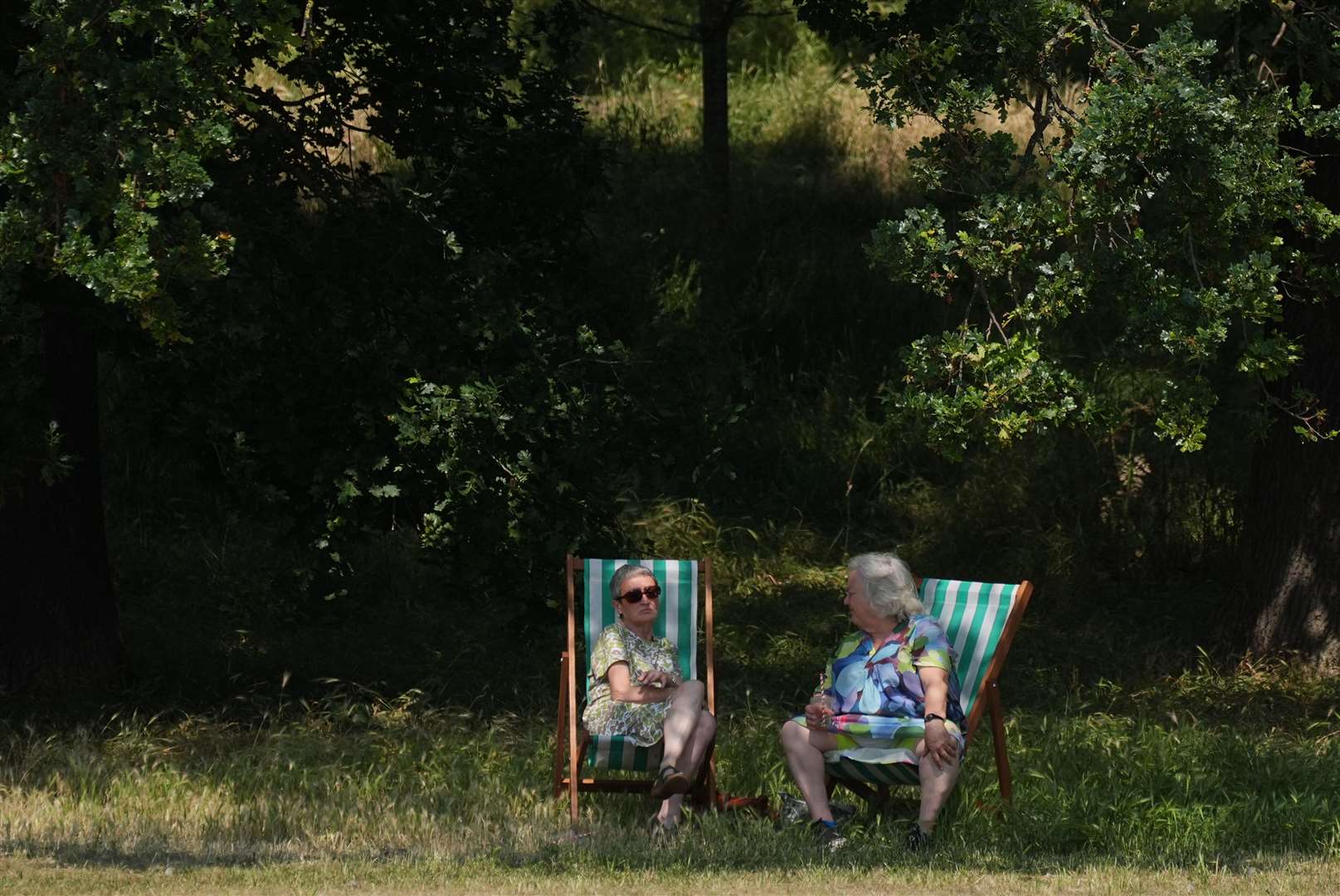 A man and a woman sitting on deck chairs in the shade (Yui Mok/PA)